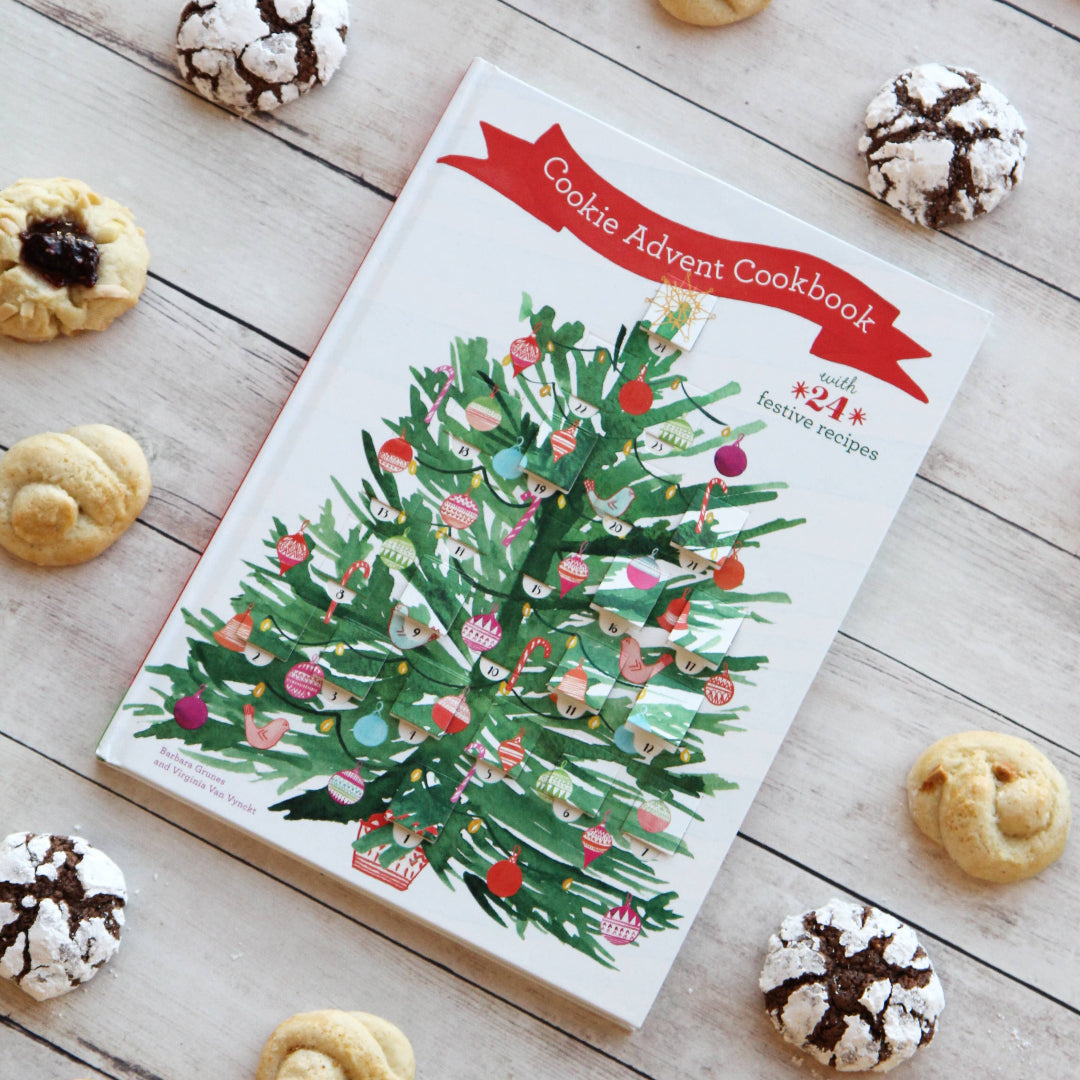 Cookie Advent Cookbook with Christmas tree design on a wooden surface with cookies around it