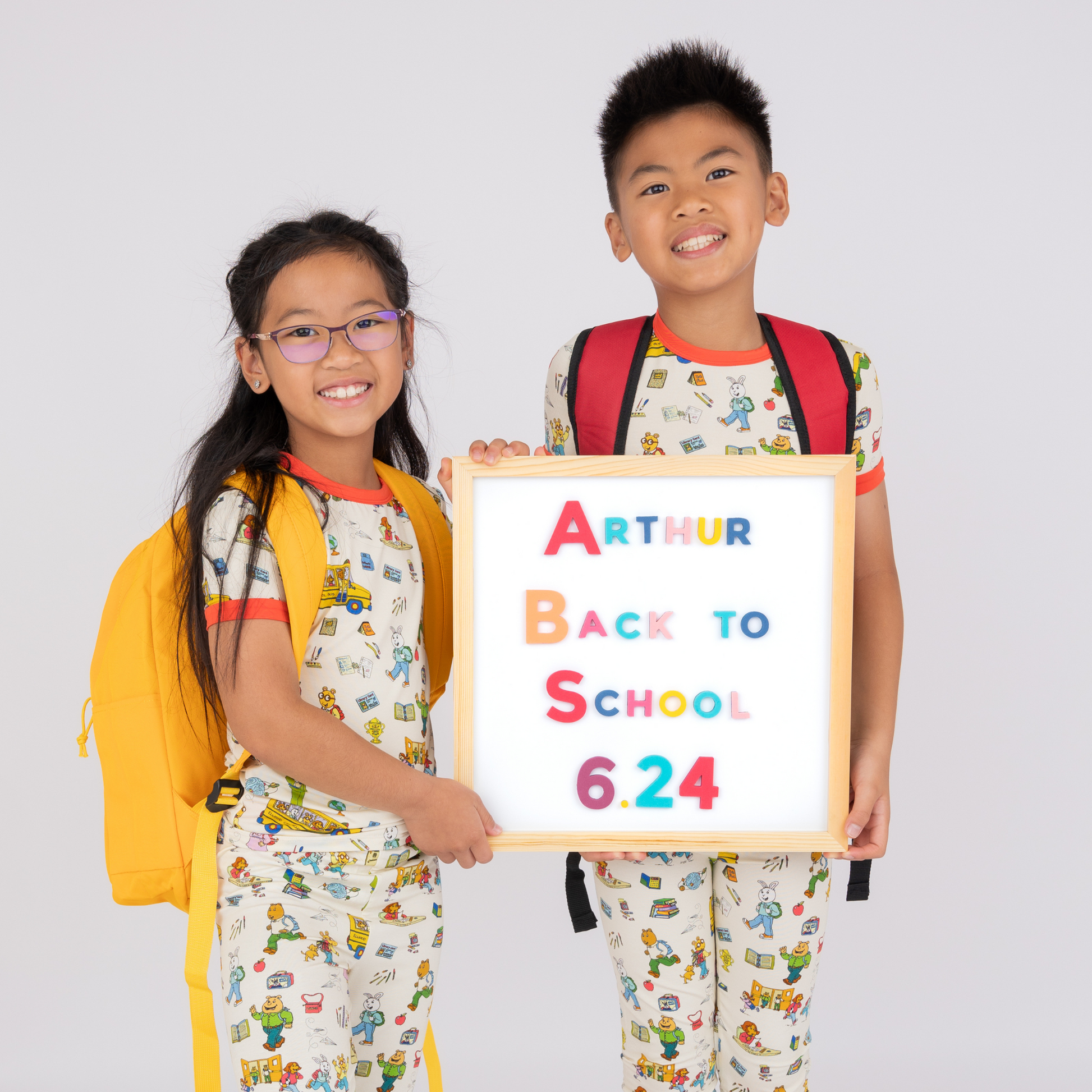 Two children in matching Arthur™ Back To School pajama sets holding a sign with 'Arthur Back to School' and a date.