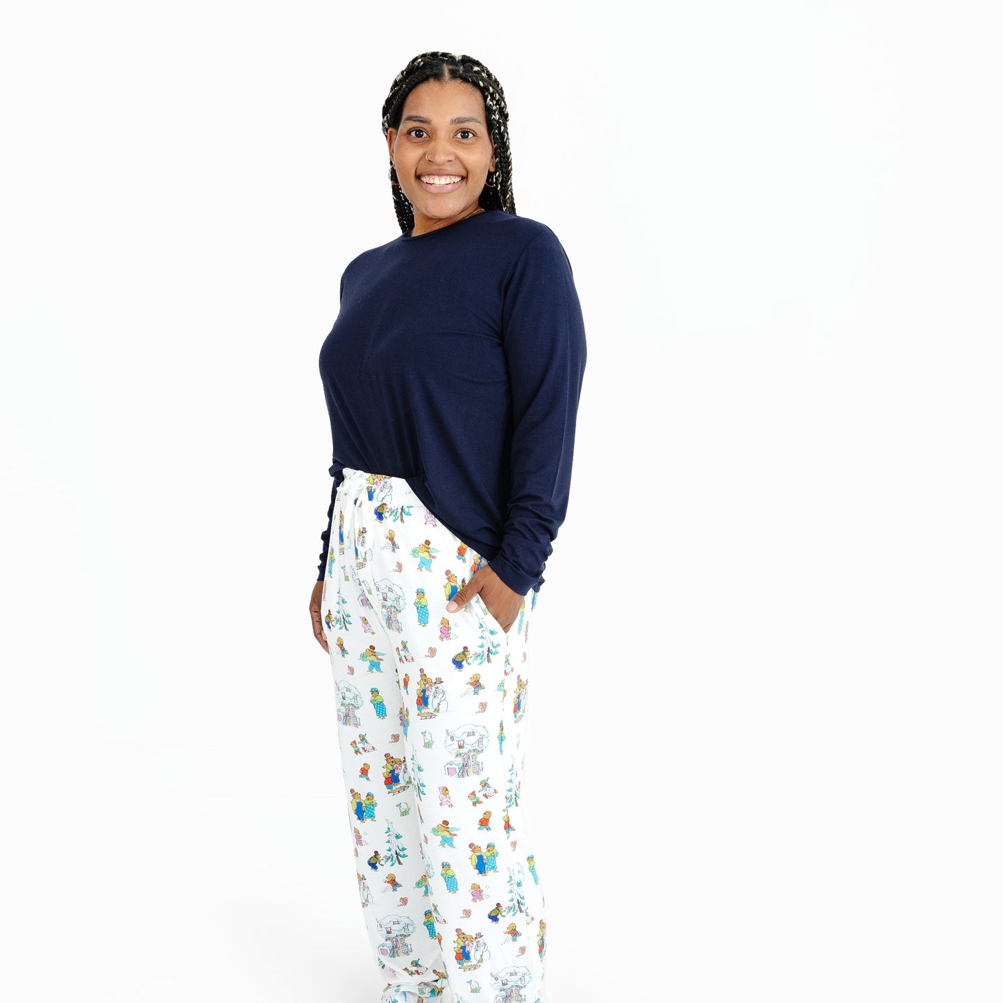 Woman wearing a navy long-sleeve top and Berenstain Bears Snow Day pajama pants on a white background