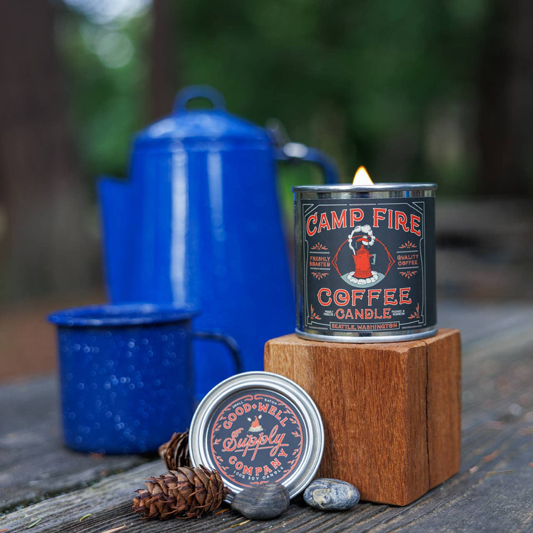 Campfire coffee candle with blue enamelware and pinecones on a wooden surface