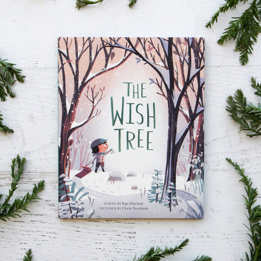 Book titled 'The Wish Tree' surrounded by greenery on a white surface