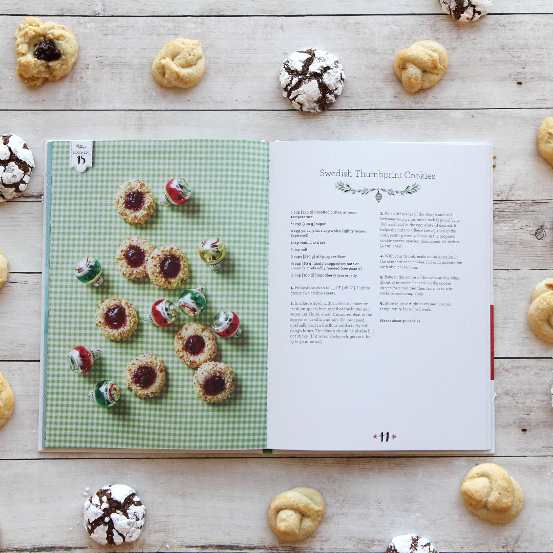 Cookbook open to a page with cookie illustrations surrounded by actual cookies on a wooden surface