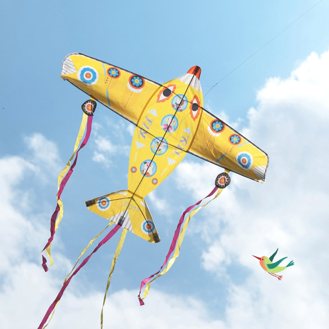 A giant flag shaped like an airplane and its yellow with streamers that fly from its tail and wings