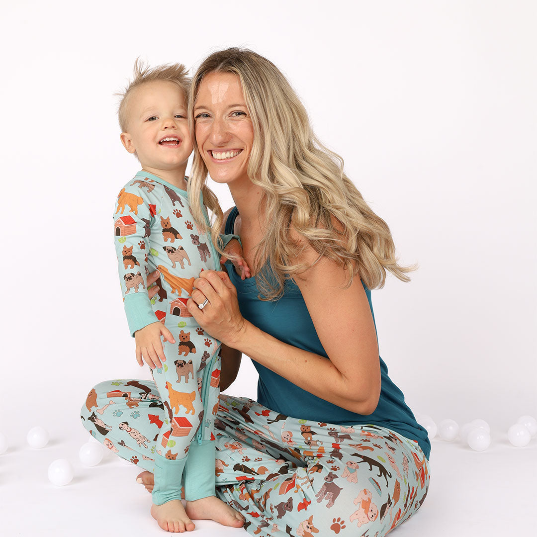 Mom and son are modeling lounge pants and convertible zippy PJ while hugging and smiling.Print is blue featuring different types of dogs, a dog house, paw prints, bones, and more!
