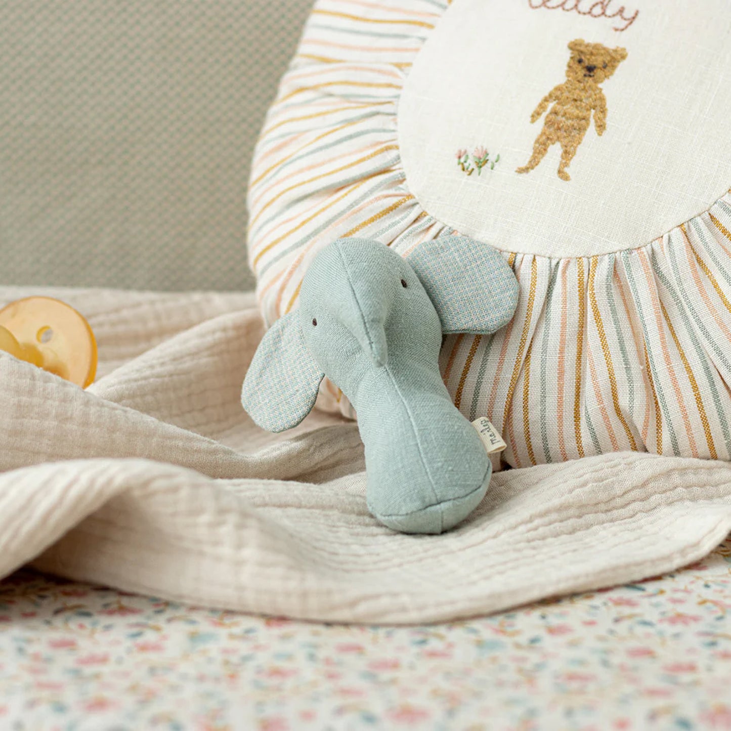 Light blue elephant plush toy on a soft blanket with a striped pillow in the background