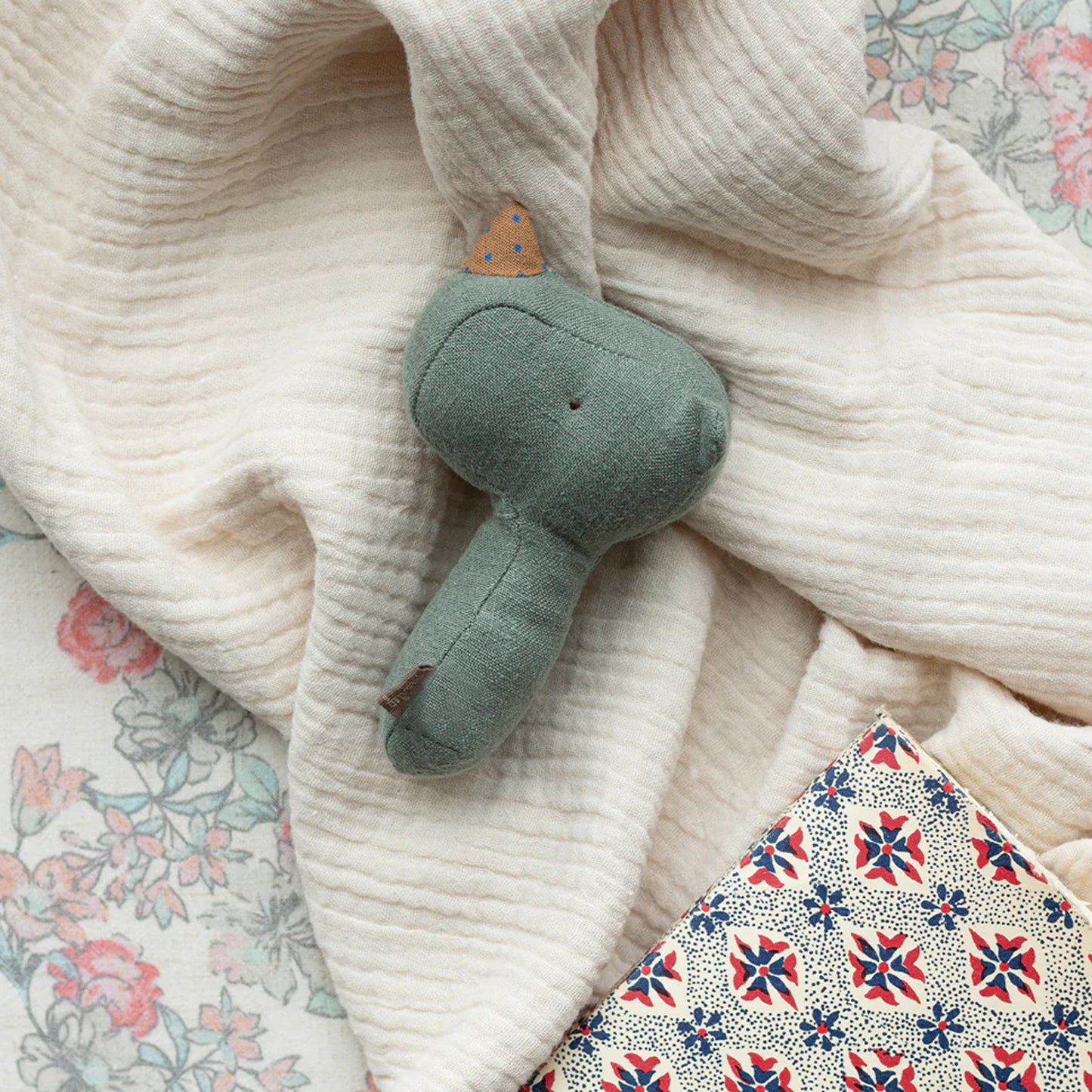 Plush elephant toy on a textured blanket with floral patterns