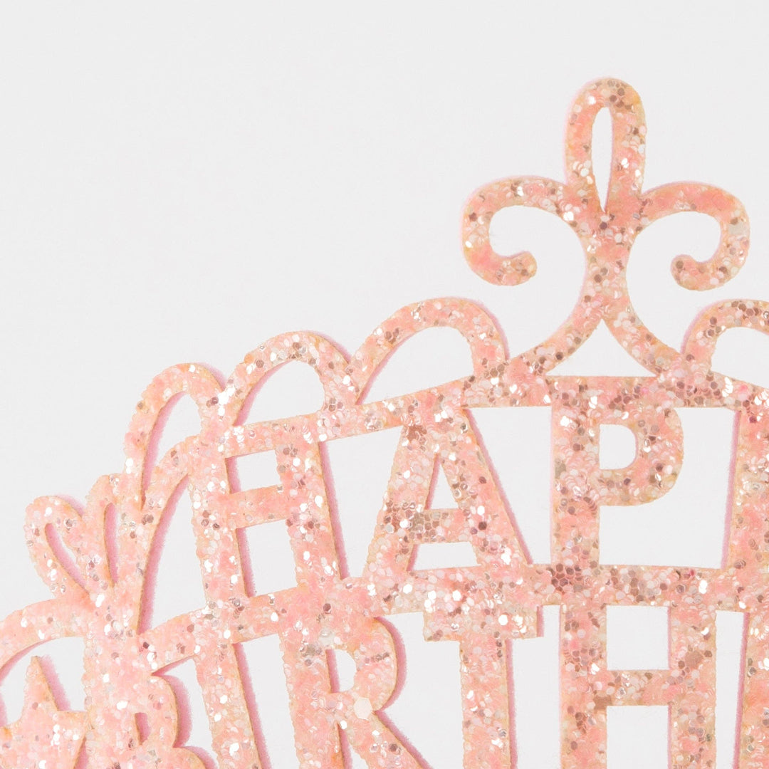 Pink glittery 'Happy Birthday' cake topper on a light gray background