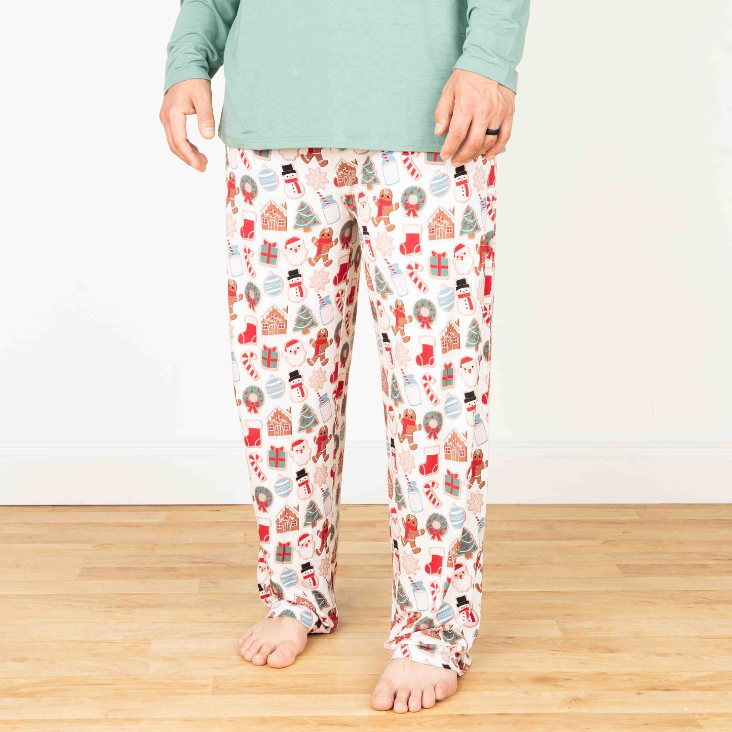 A person standing wearing Christmas-themed bamboo lounge pajama pants with a variety of festive prints including cookies, presents, and holiday decorations.