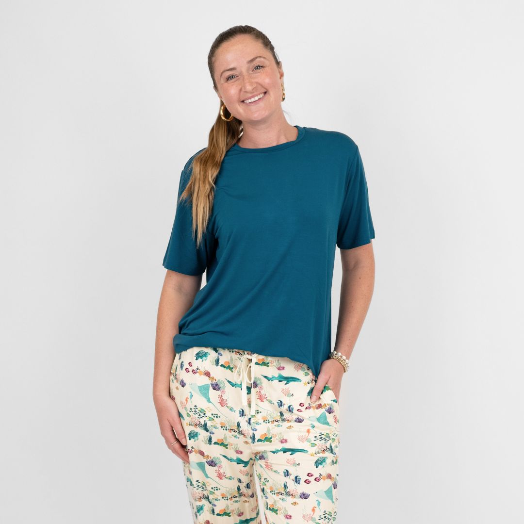 Woman wearing a blue bamboo t-shirt and patterned pants on a plain background