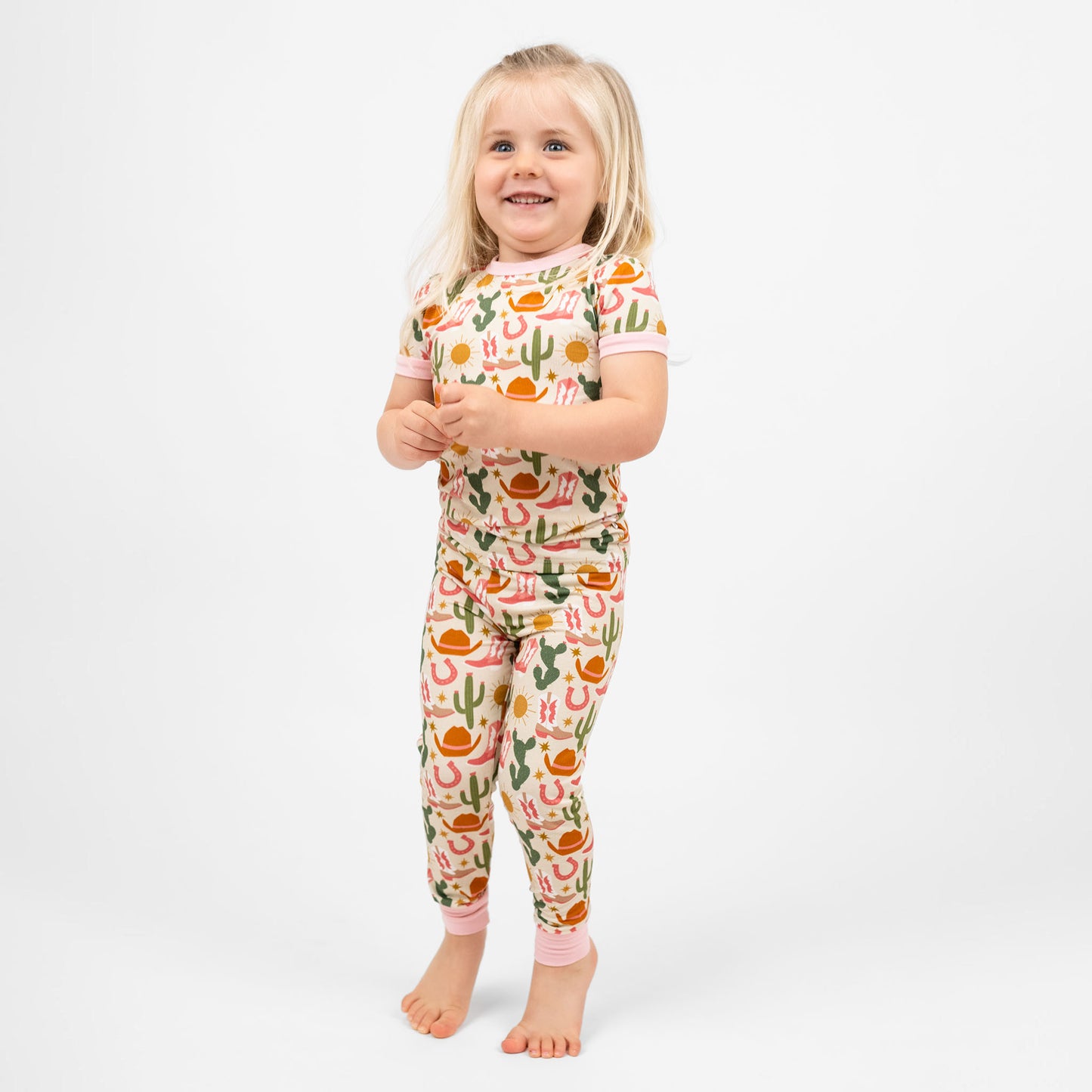 A happy young girl wearing a cute cactus-patterned pajama set, radiating joy in her Hey Y'all Western Bamboo Short Sleeve Kids Pajama Pants Set.
