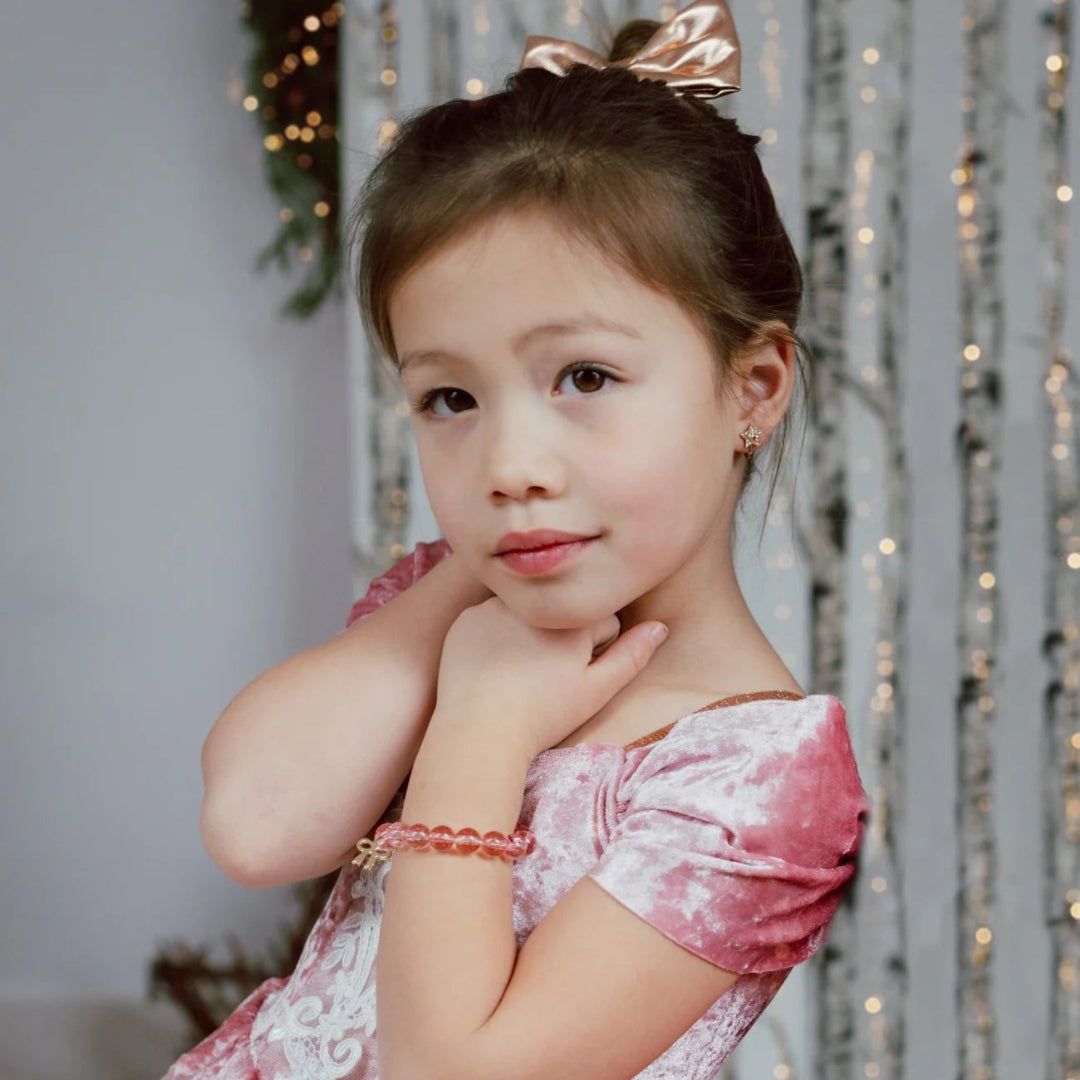 Young girl in a pink dress with a bow in her hair wearing the red and white beaded bow charm bracelet from Great Pretenders