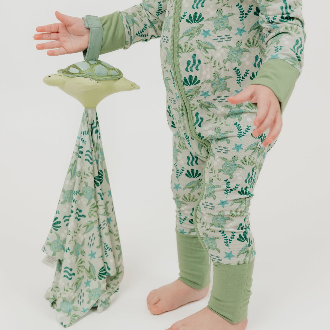 A toddler holds our Save the Sea Turtle lovey, featuring a plush turtle attached to a cozy, ocean-inspired printed blankie. Made from ultra-soft bamboo, this comforting lovey is perfect for snuggles and soothing moments.