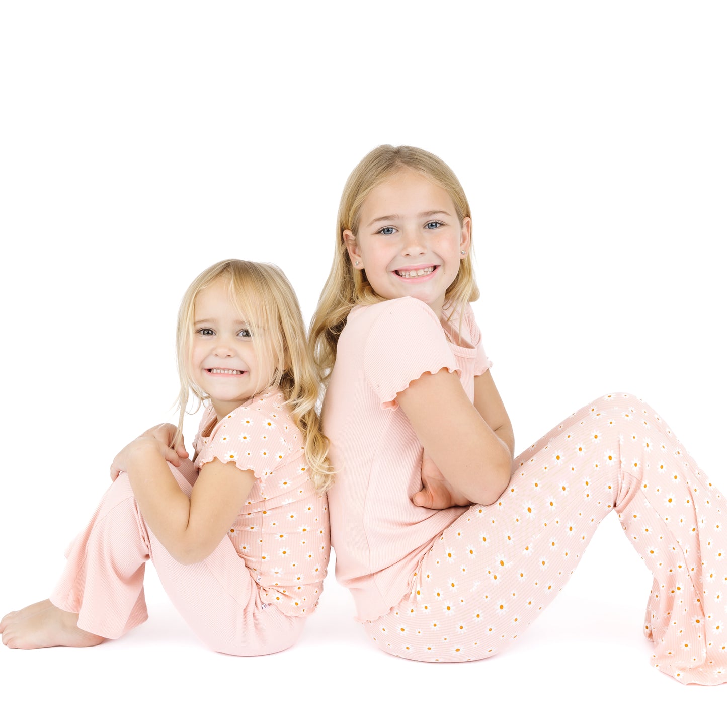 Two young girls wearing matching pink pajamas with a white background