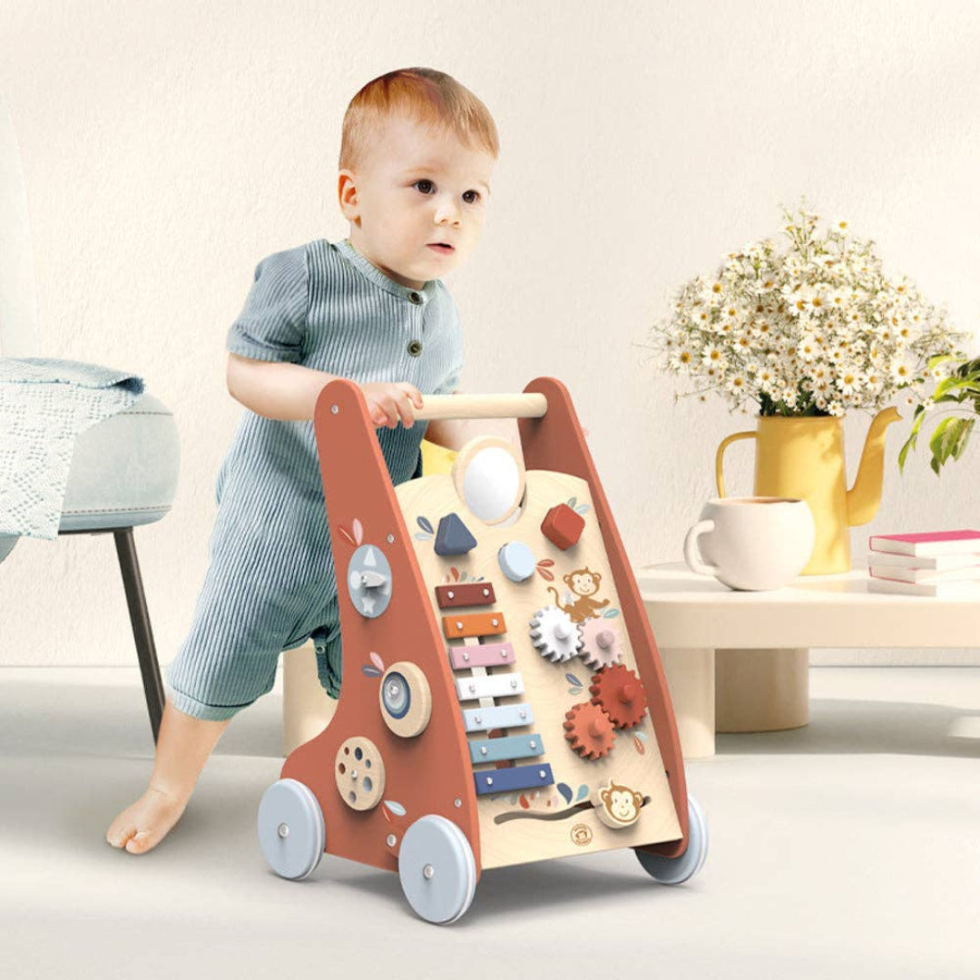 a baby pushing a multicolored walking in a house with a table with flowers on top in the background