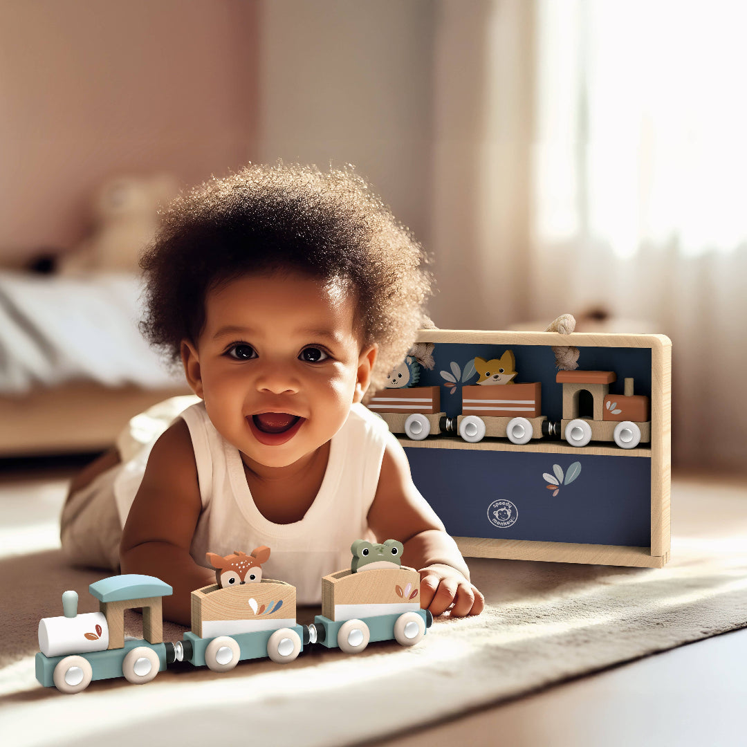 a little. baby laying on the floor playing with a wooden toy train in a bedroom