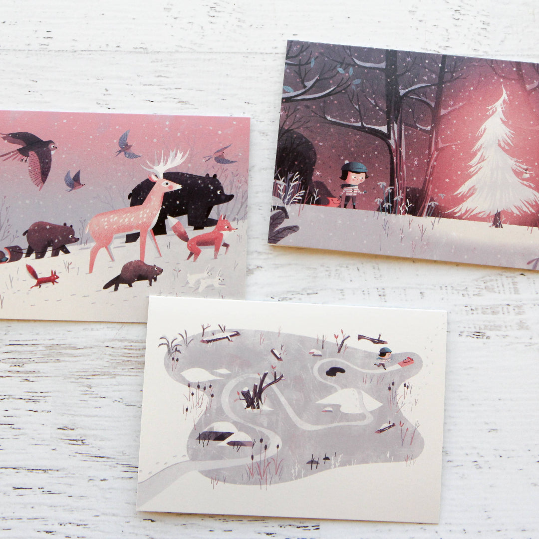 Three illustrated greeting cards featuring animals and nature scenes on a wooden surface.