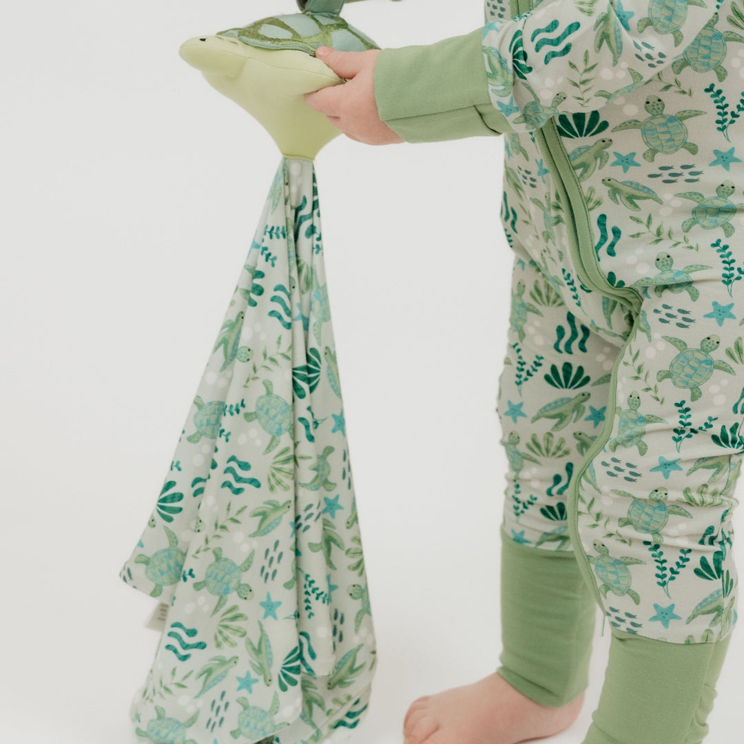 A toddler holds our Save the Sea Turtle lovey, featuring a plush turtle attached to a cozy, ocean-inspired printed blankie. Made from ultra-soft bamboo, this comforting lovey is perfect for snuggles and soothing moments.