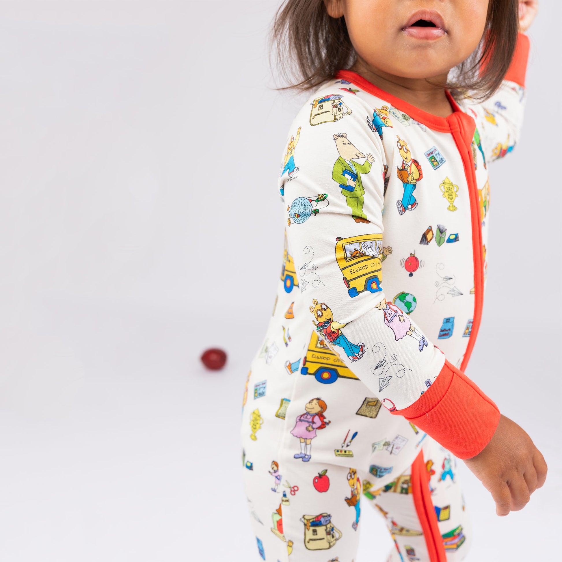 Close up on our buttery-soft  bamboo convertible pajama featuring red trims and playful illustrations of Arthur™ PBS Character, books, and school bus, a beige background.