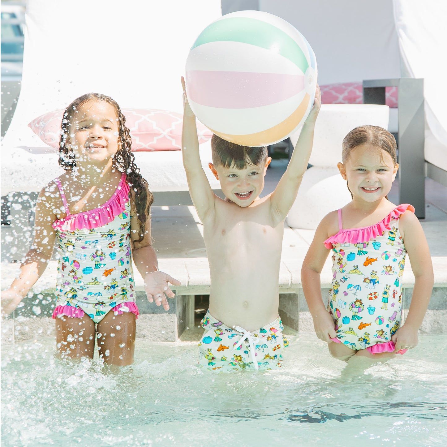 Siblings playing in the pool with our Arthur's Family Vacation one piece and swim trunks with a playful print of Arthur™ in swimwear surrounded by fun beach props — perfect for family getaways.