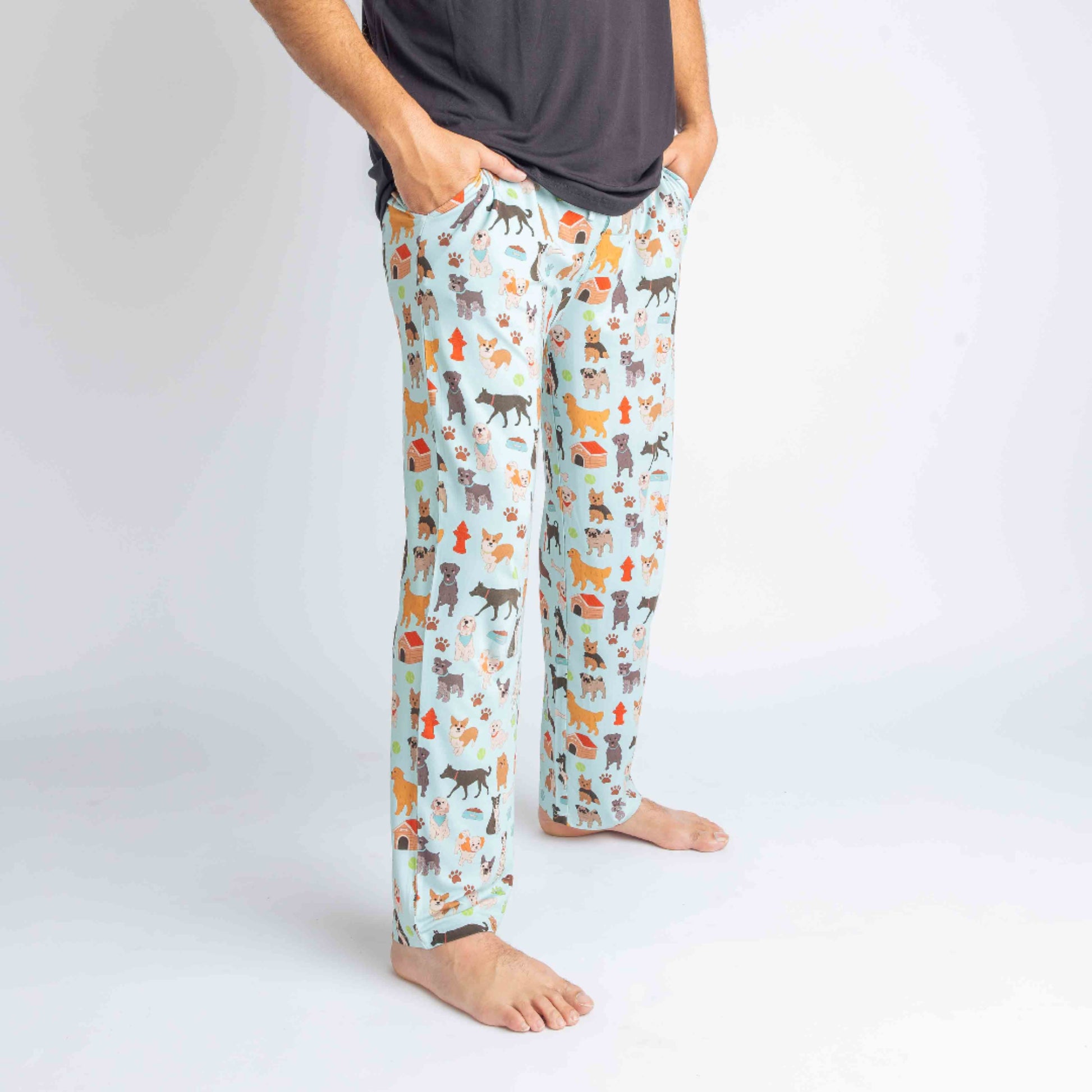 Close up of a man wearing the "dogs bark" relaxed pants. the "dogs bark" print is a mix of various types of dogs, dog houses, dog bones, paw prints, dog food, and tennis balls scattered around a light blue background.