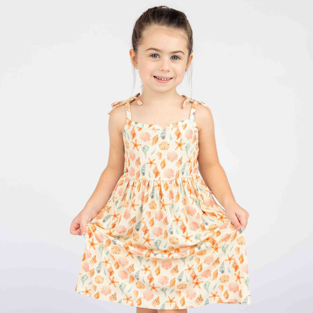 Girl smiling and posing with our Sandy Seashell Sundress in a white background.