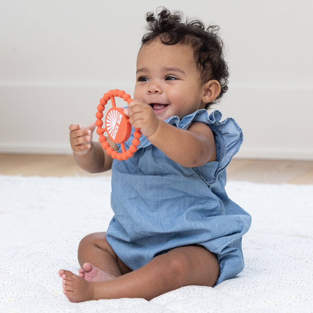 little baby with round orange baby teether with the words beach bum written in white letters on the front