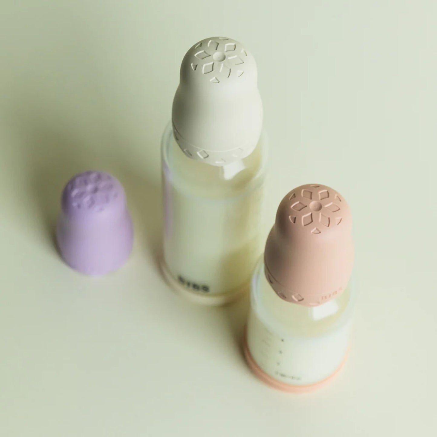 Three glass baby bottles with floral designs on the caps on a light background