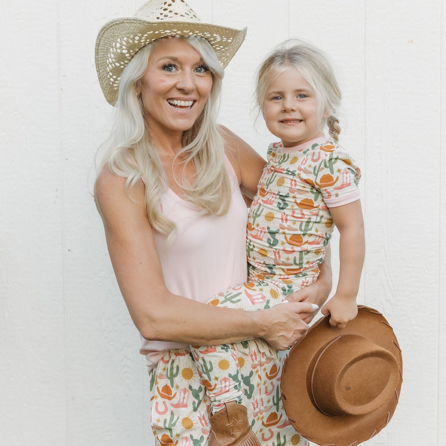 Woman and child in matching outfits with a straw hat against a white background