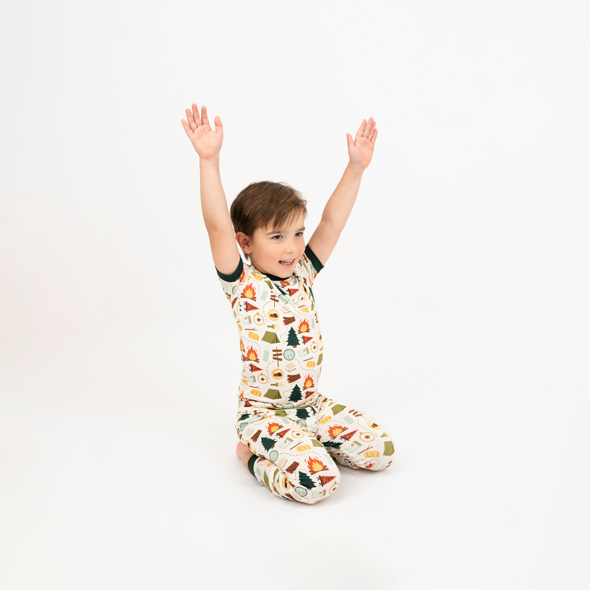 Child sitting on the floor with arms raised while wearing Camp Emerson print bamboo pajamas.