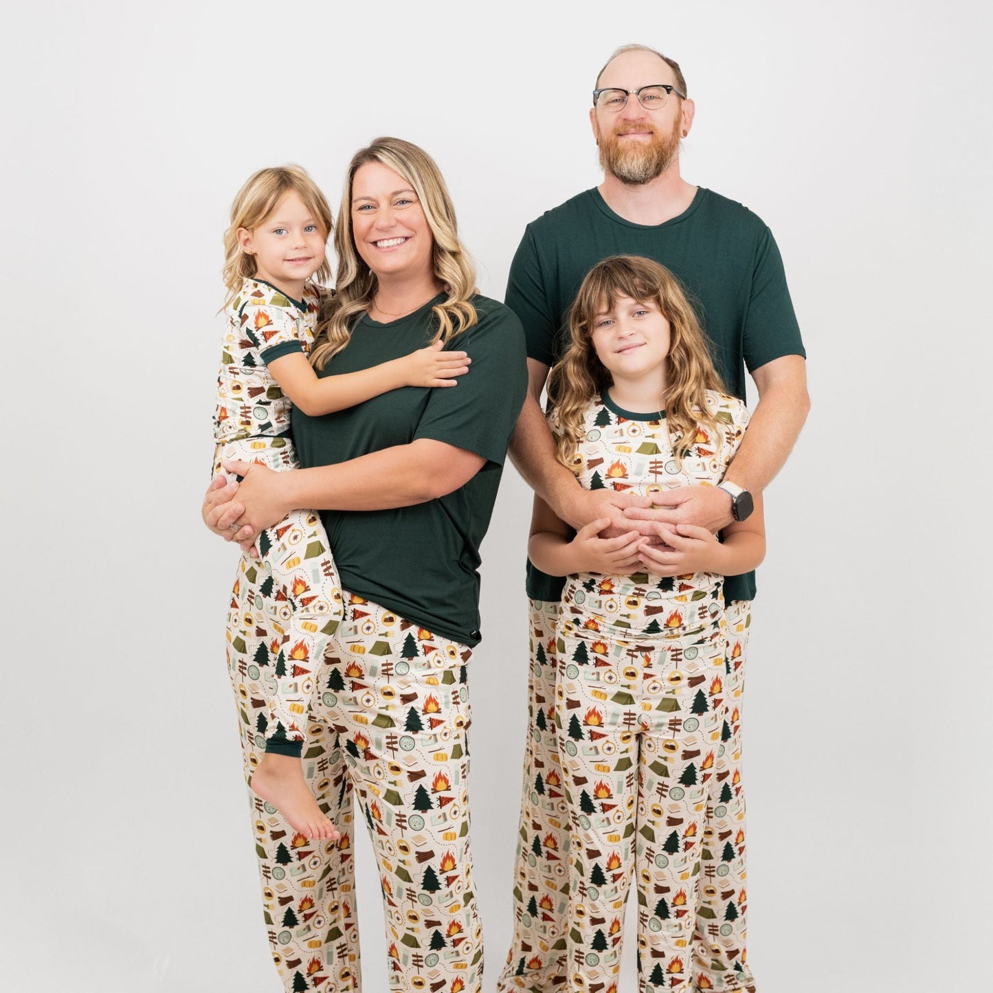 Family of four wearing Camp Emerson matching pajamas with nature-themed design on a plain background