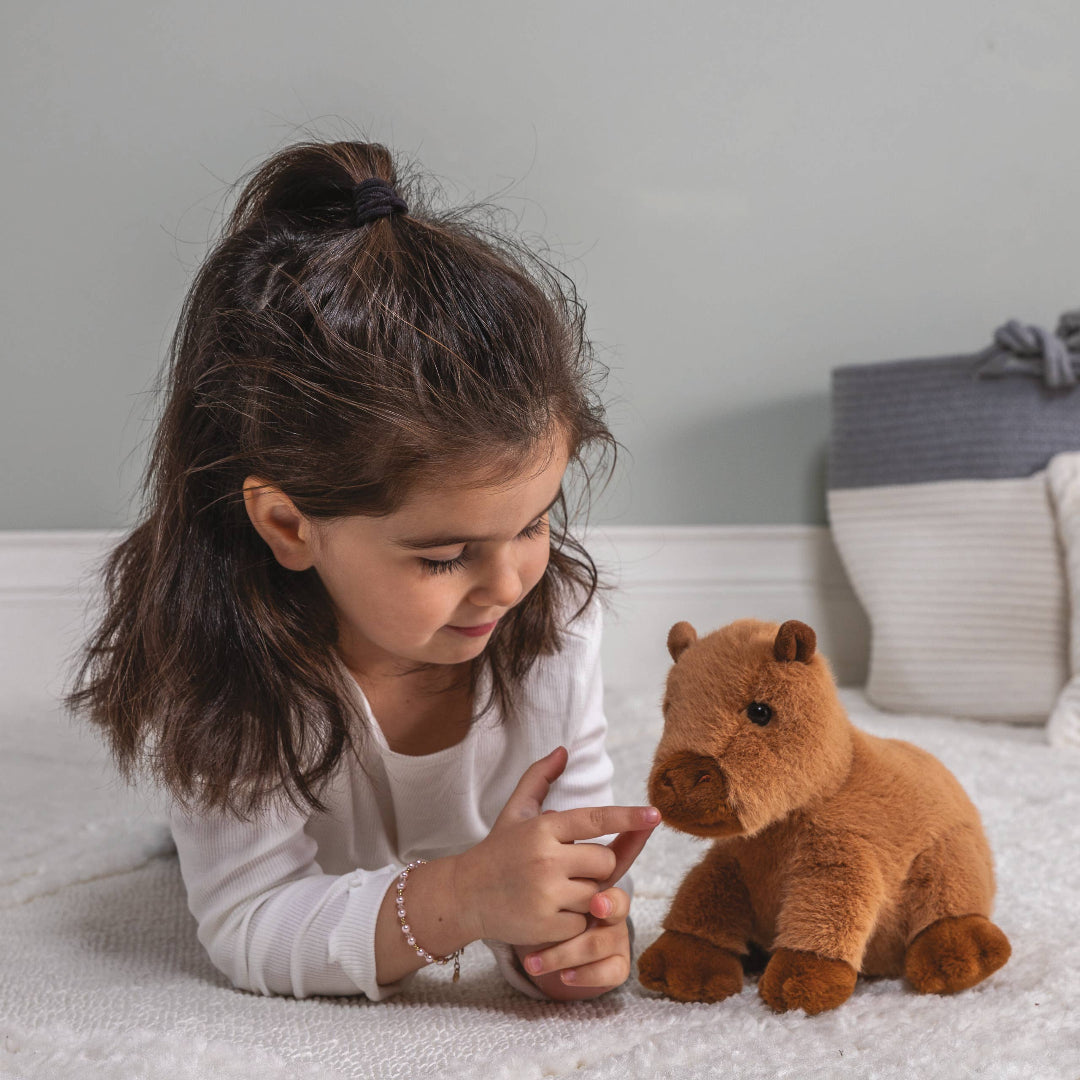 little girl playing with brown capybara stuffed toy
