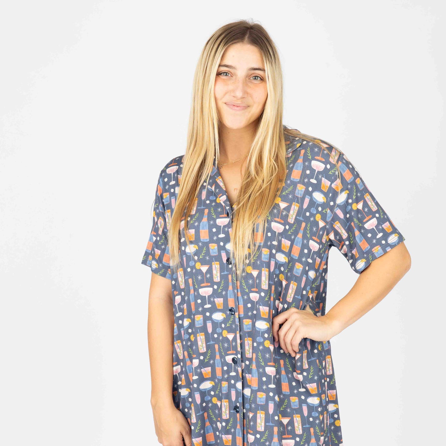 A woman wearing a short-sleeved multicolor nightgown with a geometric pattern, buttoned at the top, standing against a neutral background.