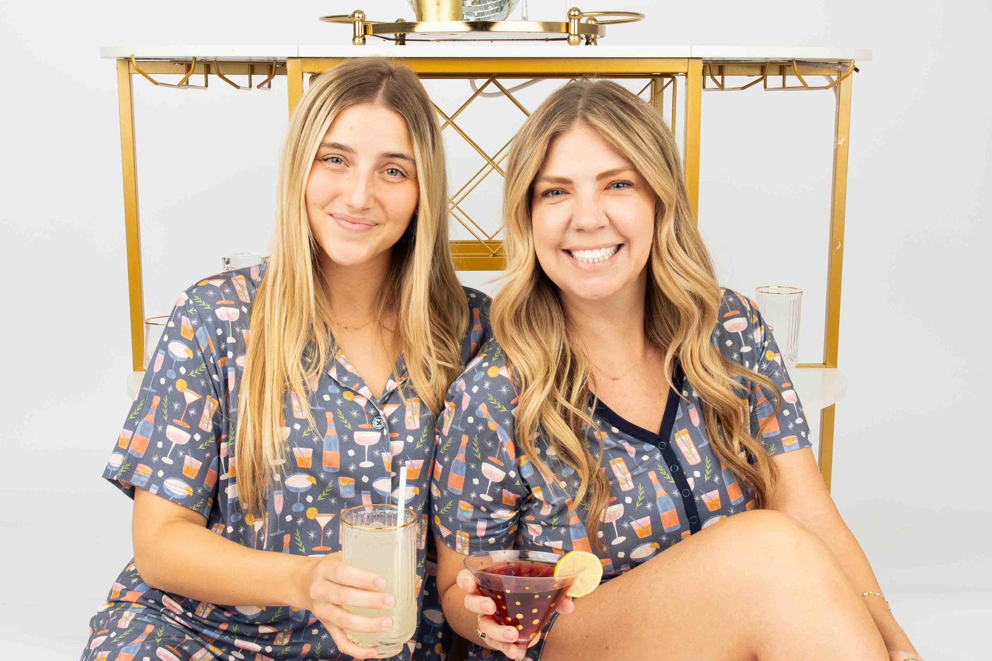 Two women in matching pajamas sitting  with drinks.
