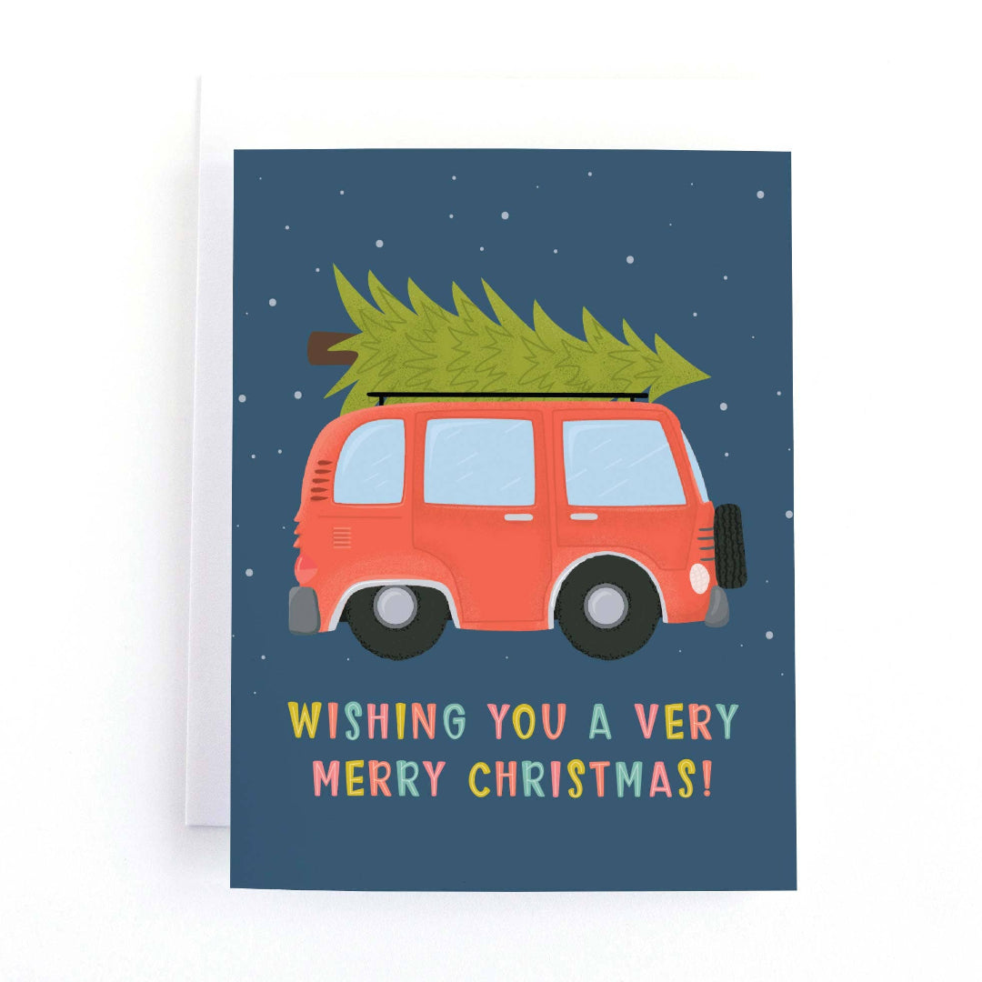 christmas card with a red van hauling a christmas tree that says wishing you a very merry christmas