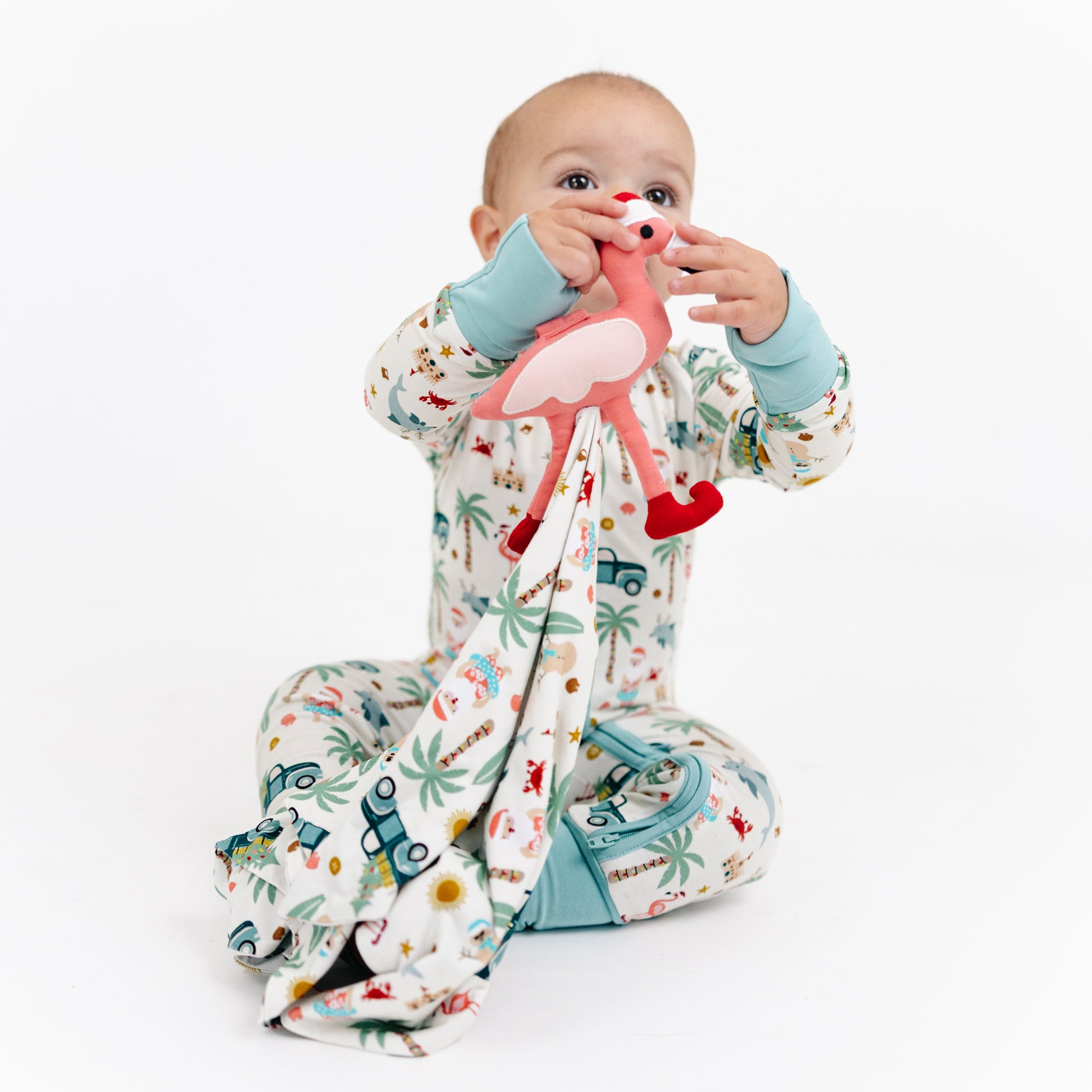 Baby in a patterned onesie holding a flamingo toy on a white background