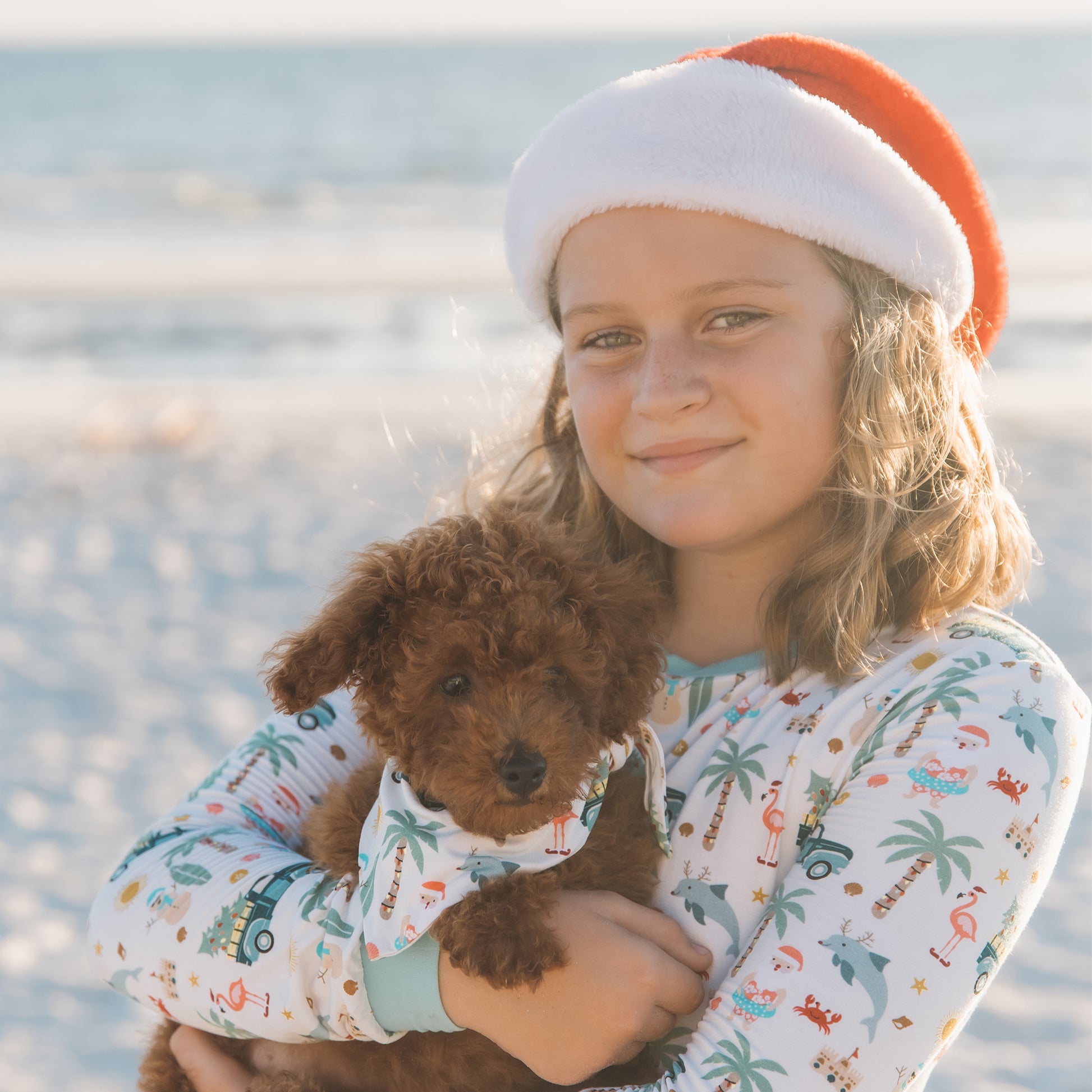 Child wearing a Santa hat holding a teddy bear on a beach