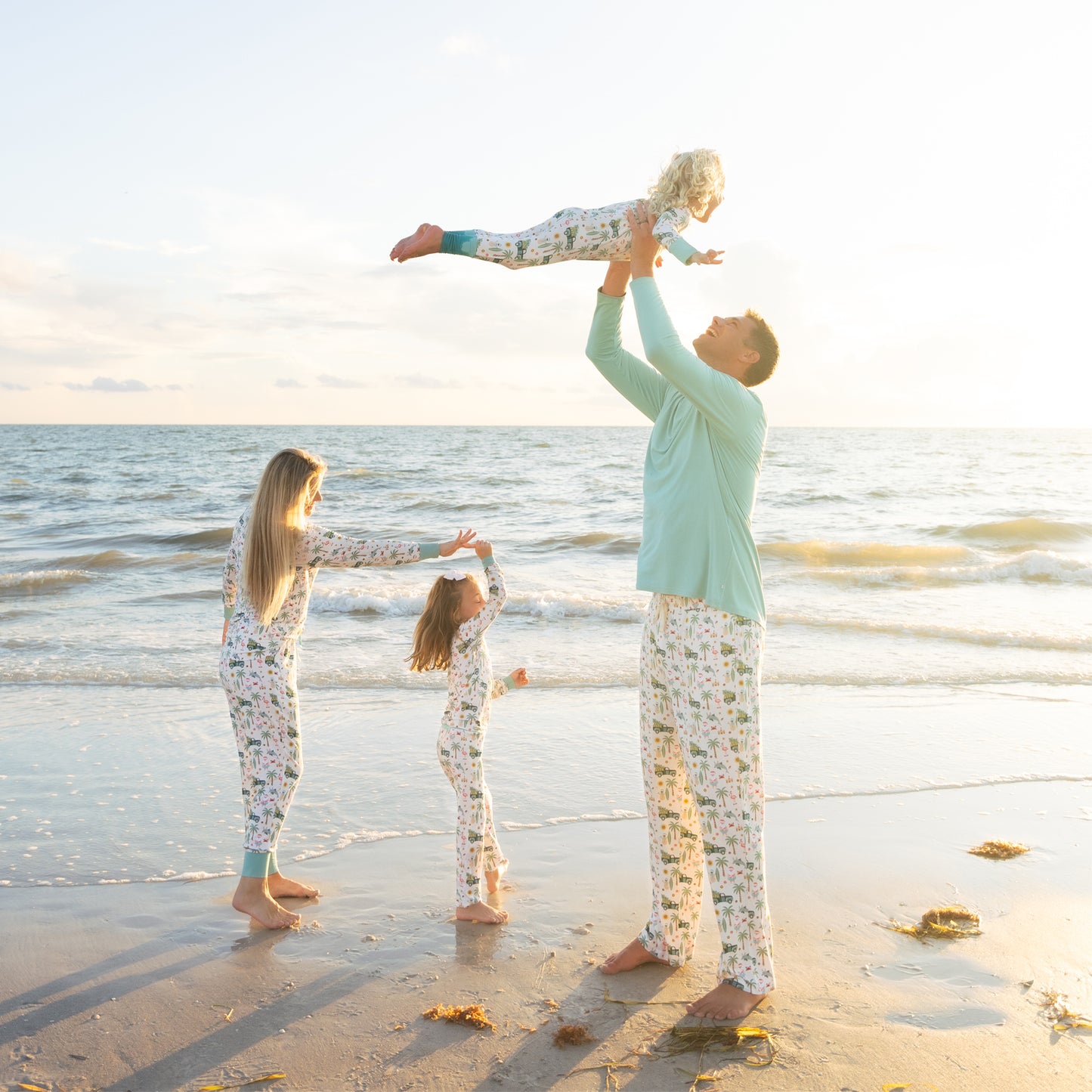 Family of four in matching pajamas on a beach at sunset