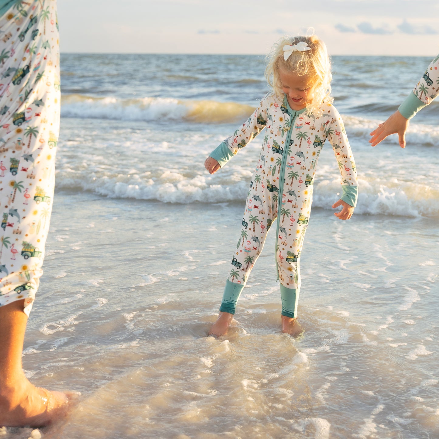 Child in a patterned convertible pajama playing in the ocean with adults nearby.