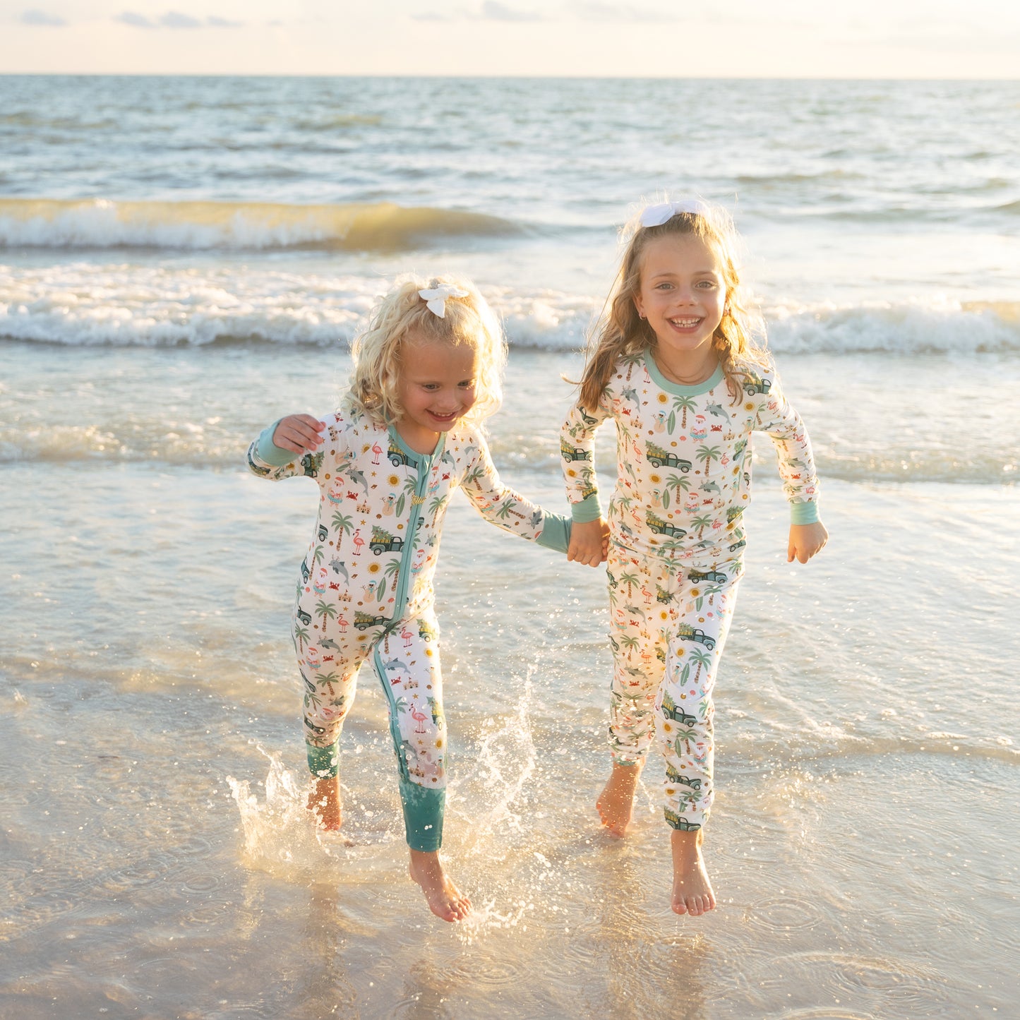 Two children in matching pajamas playing in the surf on a beach.
