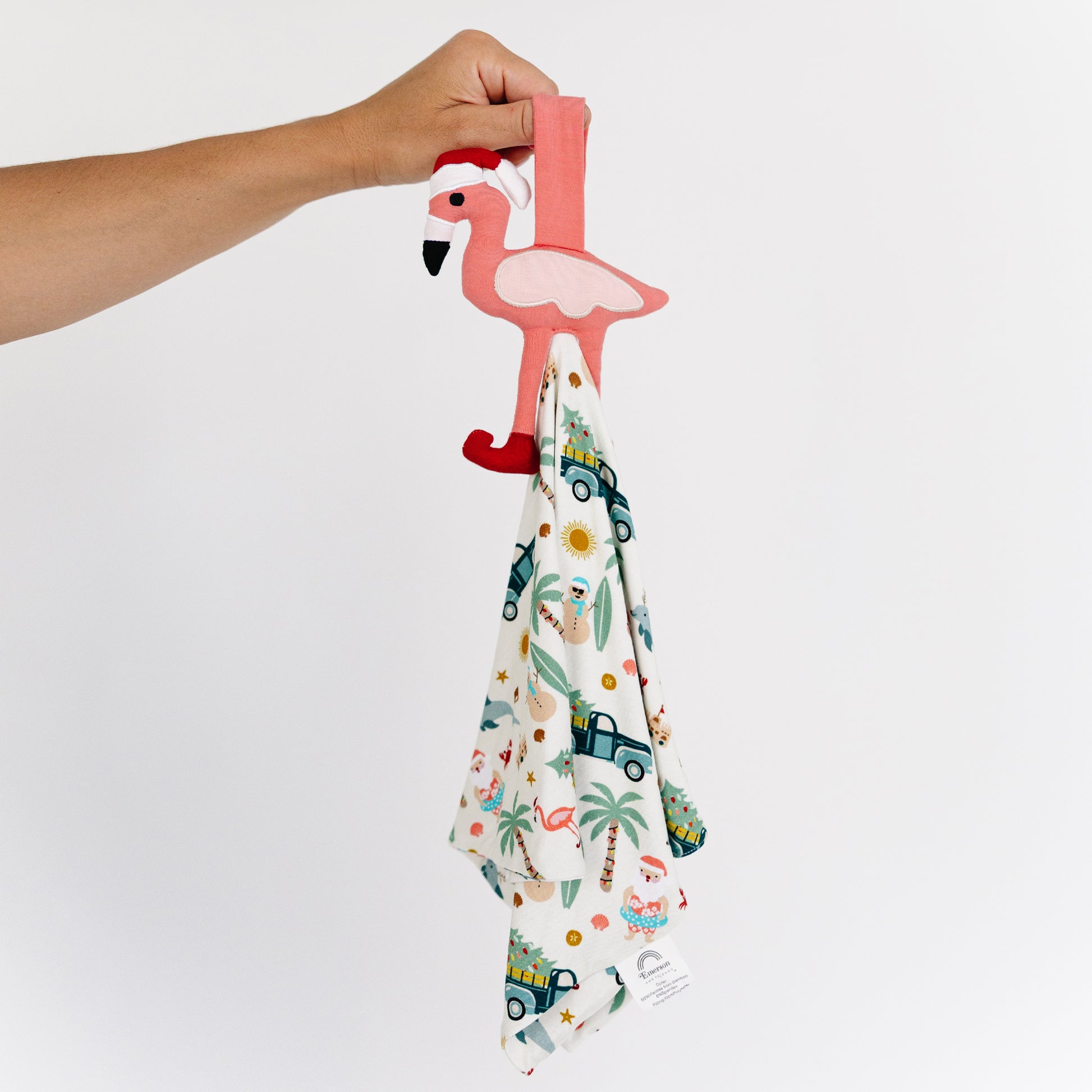 Hand holding a flamingo-shaped hook with a patterned towel underneath on a white background