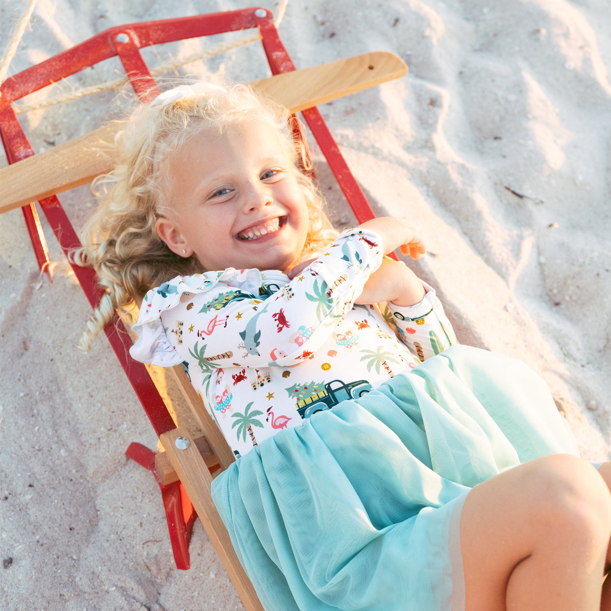 Child lying on a red and wooden beach chair on sand