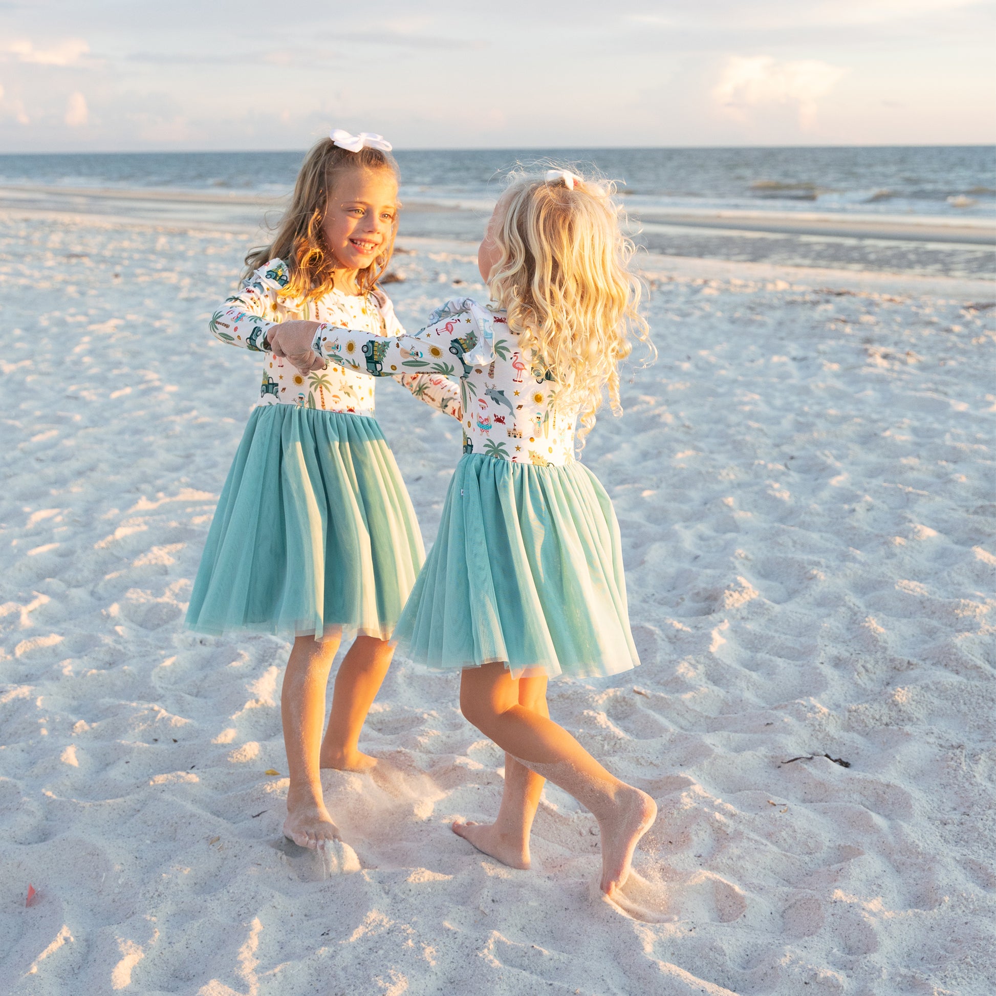 Two young girls in matching outfits standing on a sandy beach.