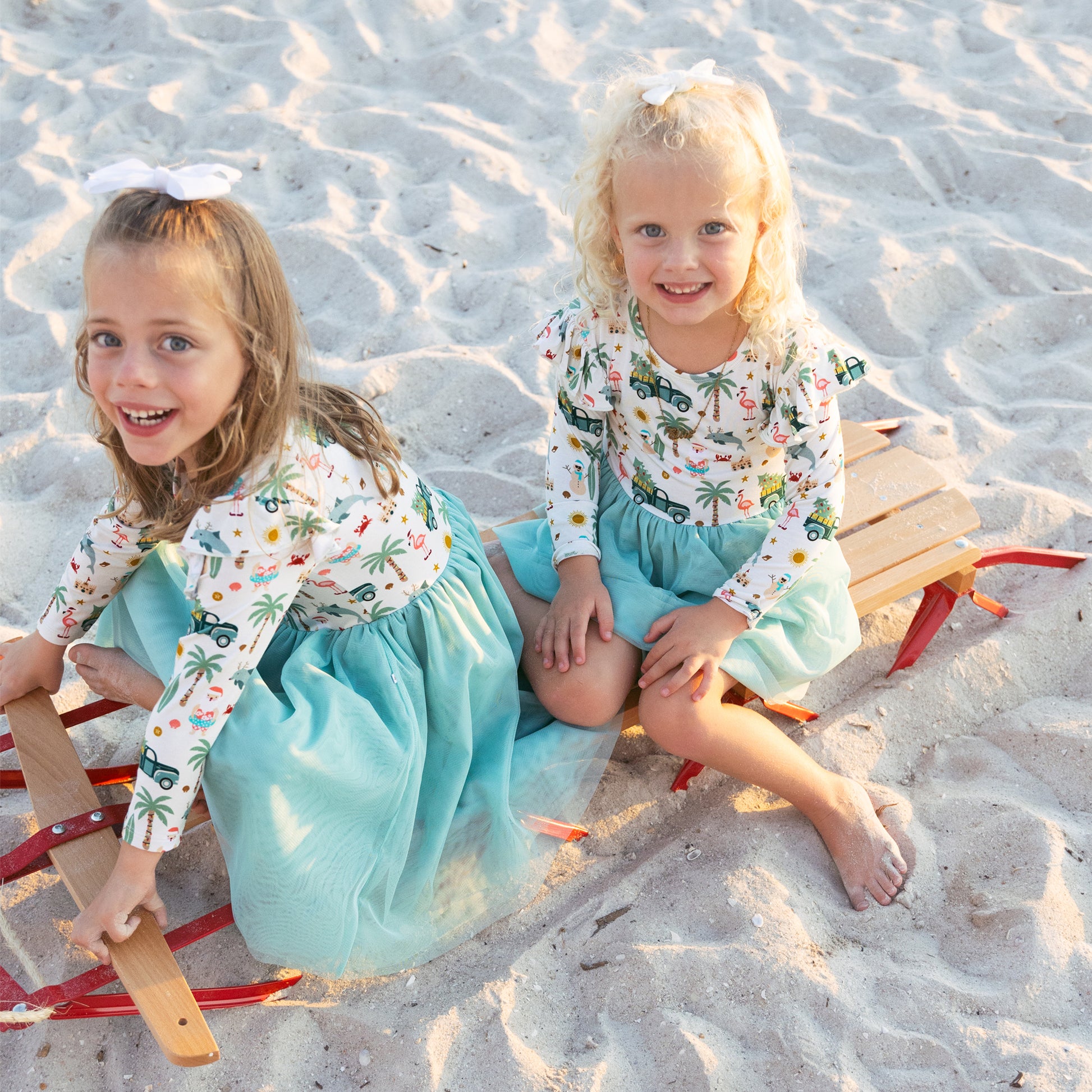 Two young girls sitting on a beach with sand toys.