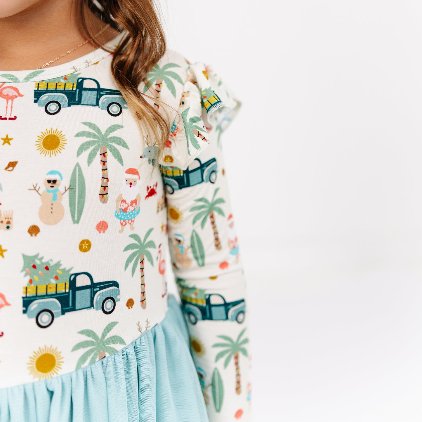 Child wearing a colorful outfit with palm trees, trucks, and other patterns on a white background