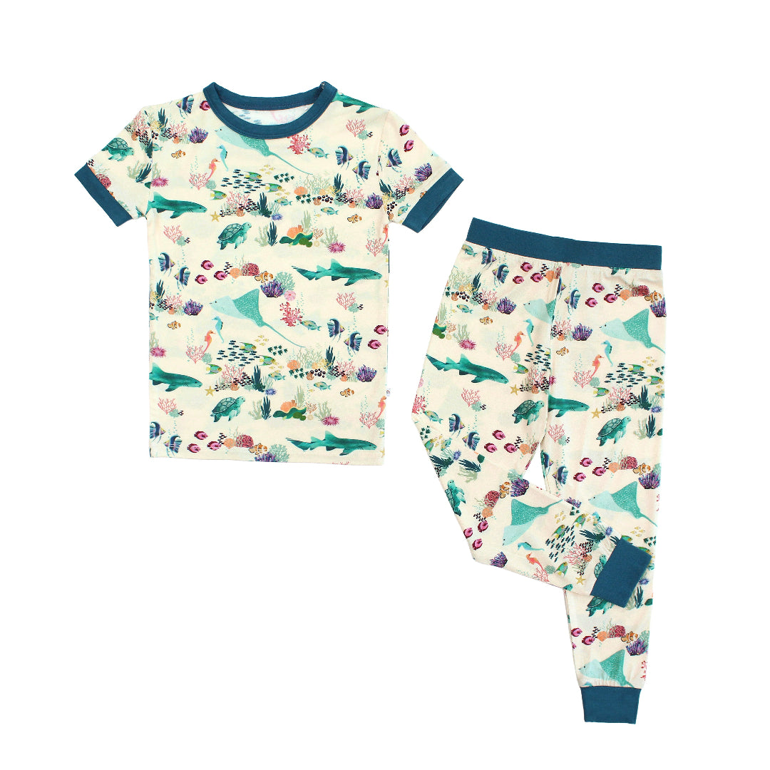 Emerson and Friends Coral Reef Bamboo Kids Pajama Set featuring a soft, breathable short sleeve top and matching pants with an ocean-inspired print of sharks, sea turtles, and coral reefs—perfect for cozy nights and sweet dreams.