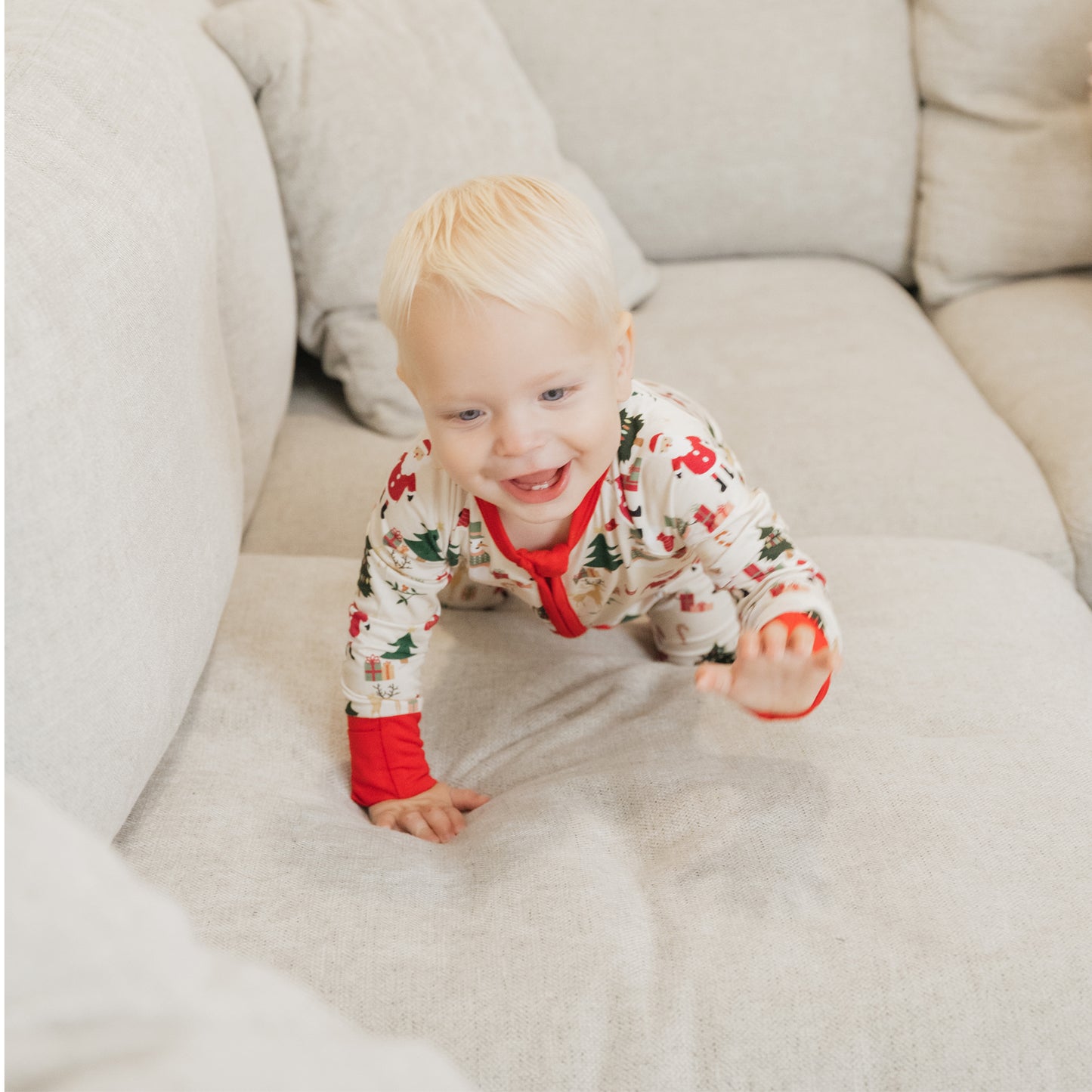 Baby crawling on a white couch in Cozy Christmas bamboo zip pajamas – buttery soft, temperature-regulating holiday sleepwear.