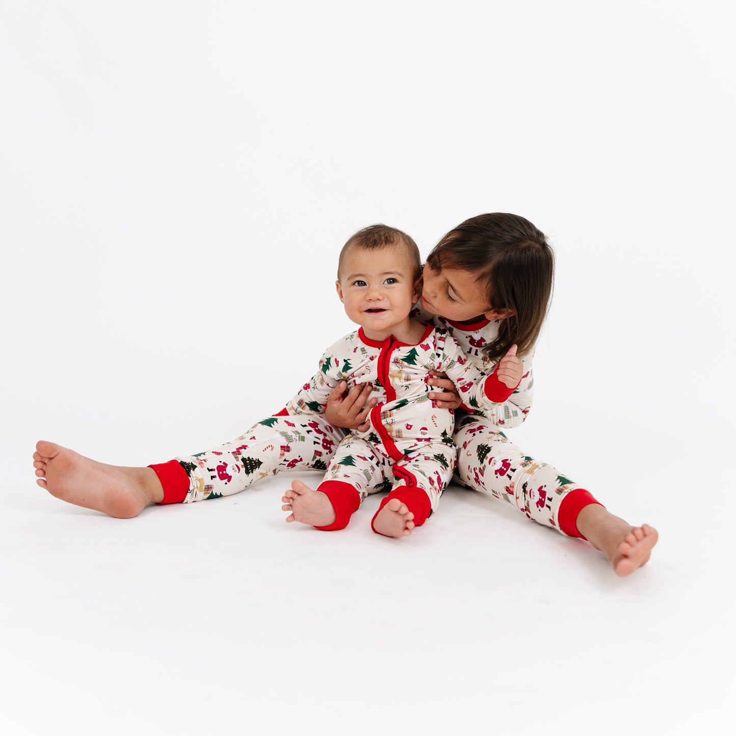 Two siblings in Cozy Christmas bamboo pajamas sitting together, showing adorable matching holiday outfits.