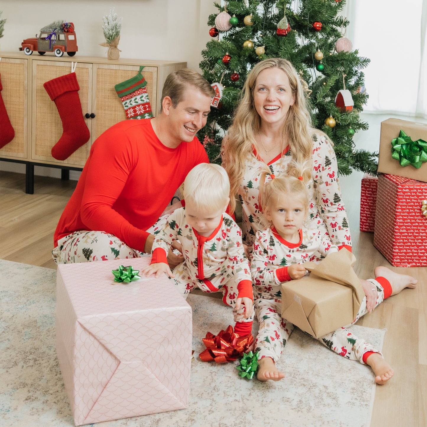 Family opens gifts by the tree wearing Cozy Christmas bamboo pajamas, showcasing festive jogger pants with red cuffs.