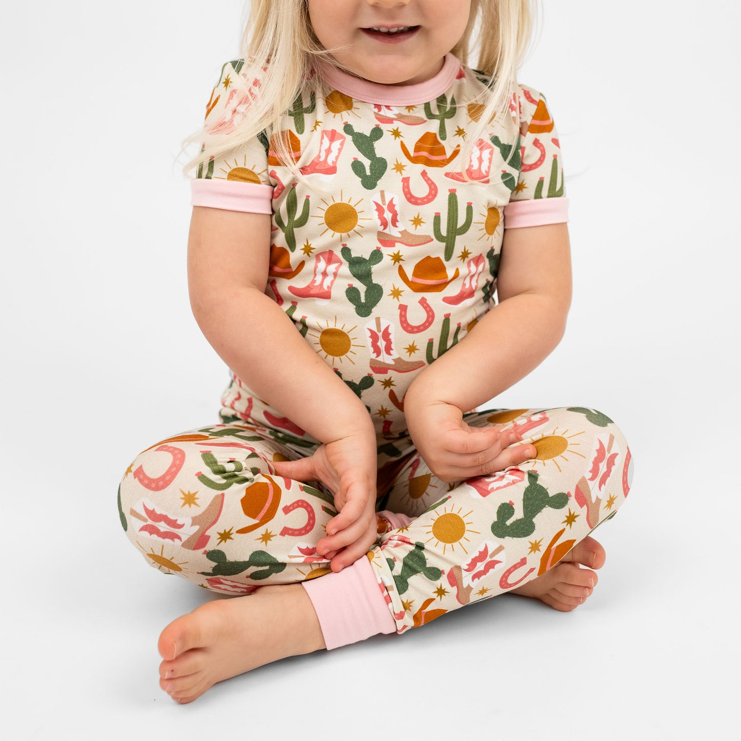 A happy girl smiling in Hey Y'all Western Bamboo Short Sleeve Kids Pajama Pants Set sitting on the floor perfect for cozy rodeo nights.