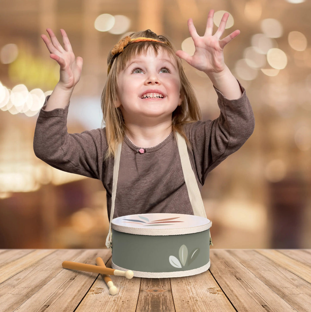 Child playing with a green drum on a wooden surface with a blurred background